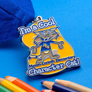 Mason Corinth Elementary Character Cat medal beside colored pencils