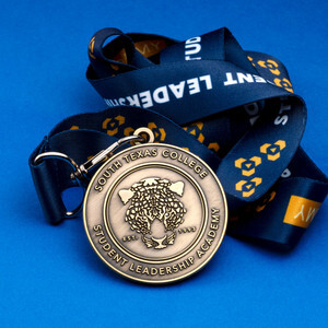 Antique brass South Texas College die struck medal on a navy lanyard