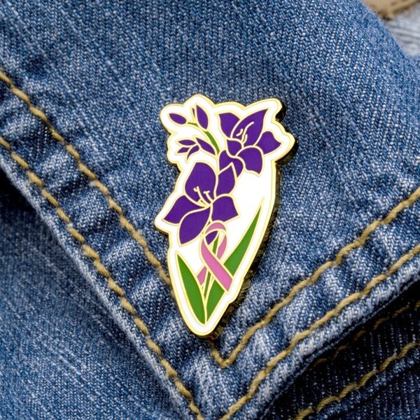 Purple gladiolus enamel pin with a pink awareness ribbon on denim